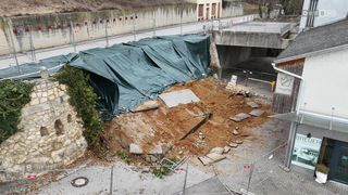 Ein Luftbild eines Baustellenbereichs mit einem grünen Planen, der Schutt, Erde und zerbrochenen Beton bedeckt, eingezäunt mit einem Schild und Absperrungen.