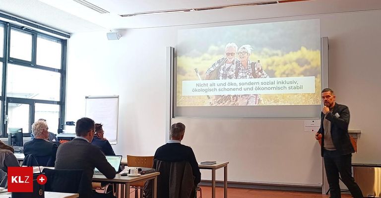 A presentation room with a projector screen displaying a motivational quote. Three men are seated at tables, with one using a laptop. A whiteboard is on the wall.