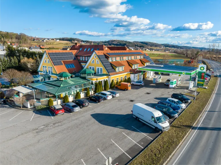 Luftaufnahme eines großen Hotels mit Solarpanelen auf dem Dach, in der Nähe einer BP-Tankstelle, mit vielen Autos vor dem Gebäude geparkt.