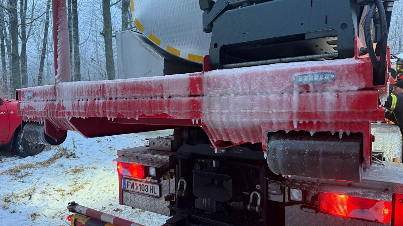 Der mit Eis bedeckte Heckstoßfänger eines Lkws ist sichtbar, das Kennzeichen FW103 HL ist angebracht. Das Fahrzeug steht auf schneebedecktem Boden, im Hintergrund sind Bäume zu sehen.