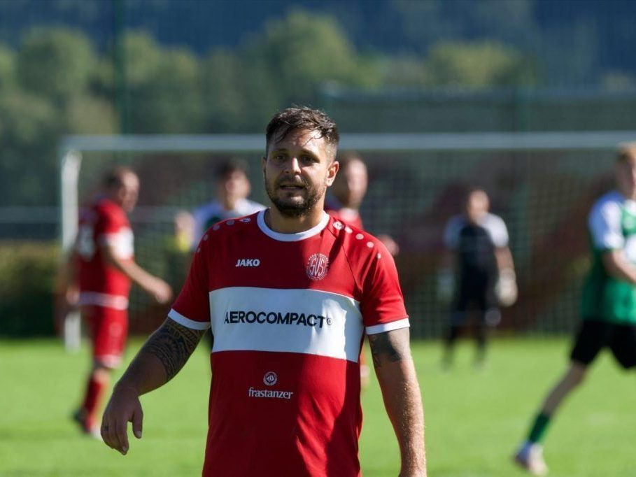A soccer player in a red Aerocompact jersey walks on the field. Other players in red uniforms are in the background.