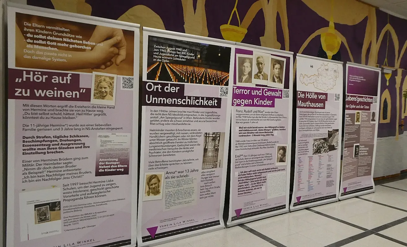 A row of posters shows information about the Holocaust, specifically the treatment of children during that time. One poster highlights the use of children in medical experiments and inhumane conditions. Another poster depicts a memorial with lit candles. The third poster shows a map of the Holocaust, indicating locations of atrocities.