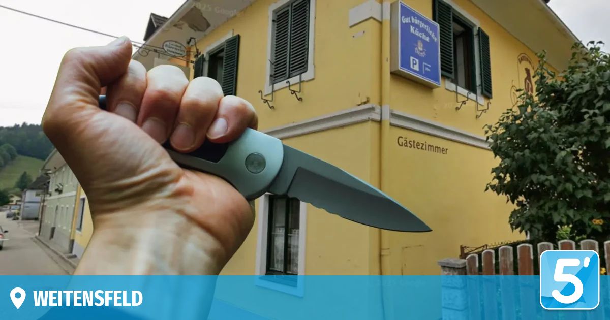 A hand holds a knife in front of a yellow building with a blue sign that reads 'Gut Burgerliche Kuche P' and a window below.