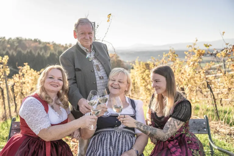 Eine vierköpfige Familie in traditioneller Kleidung, lächelt und stößt mit Wein glasses in einem Weinberg an.