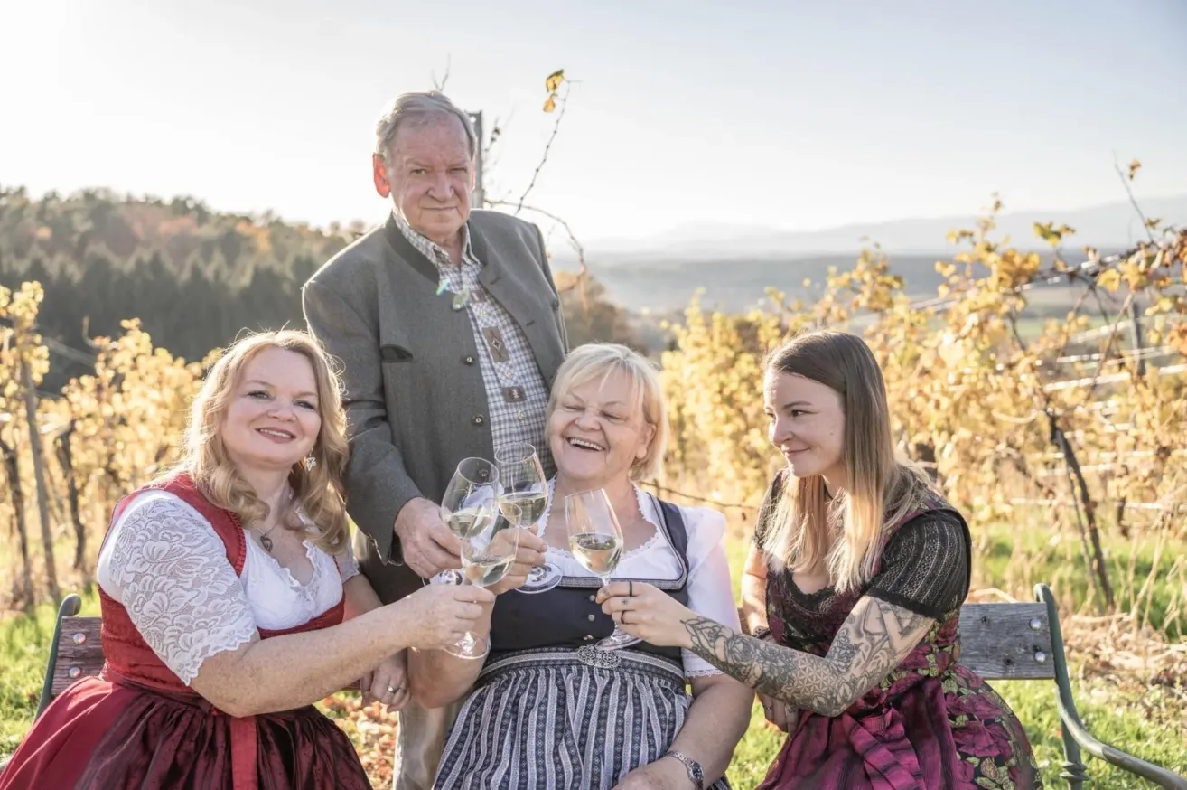 Eine vierköpfige Familie in traditioneller Kleidung, lächelt und stößt mit Wein glasses in einem Weinberg an.