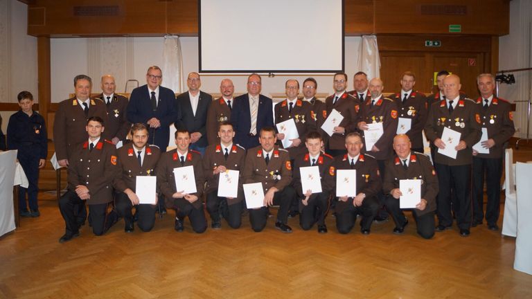 Eine Gruppe von Männern in Militäruniformen posiert für ein Foto. Einige stehen und einige knien. Sie halten Urkunden in den Händen. Sie befinden sich in einem Raum mit Holzboden.