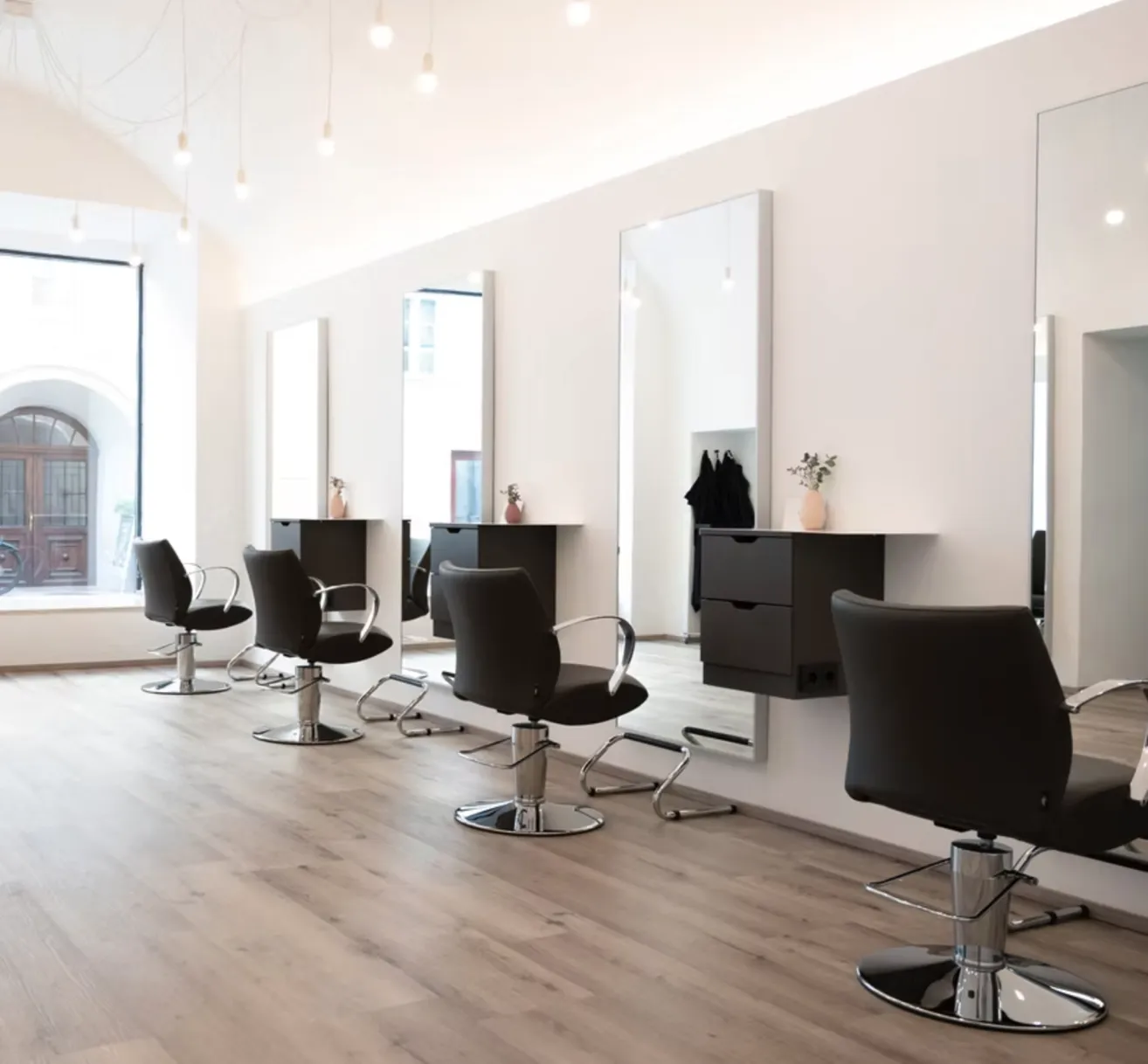 Ein leerer Salon mit Holzböden und mehreren schwarzen Stühlen mit verstellbarer Höhe. Große Spiegel sind an der Wand montiert.