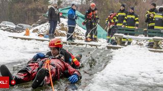 Rescuers in winter gear prepare to extract a person from icy water, holding ropes.