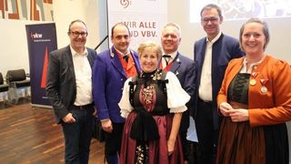 A group of adults stand together in a room with a banner and projector. They all smile and appear to be posing for a picture.