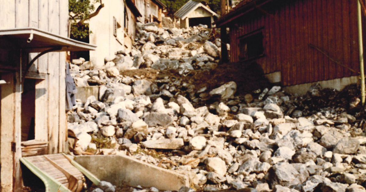An image of a landslide shows a path covered in rocks and debris, with buildings partially buried or damaged on either side.