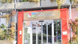 The Neue Eisenstadter office building entrance with a red facade, automatic sliding doors, and a signboard above it.