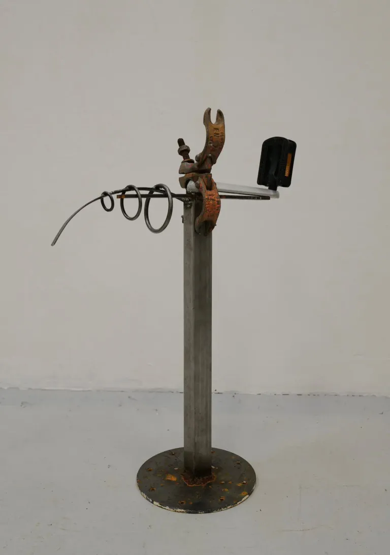 A metallic stand with various metal components like a clamp, rings, and a black rectangular object. The stand is on a gray floor.
