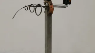 A metallic stand with various metal components like a clamp, rings, and a black rectangular object. The stand is on a gray floor.