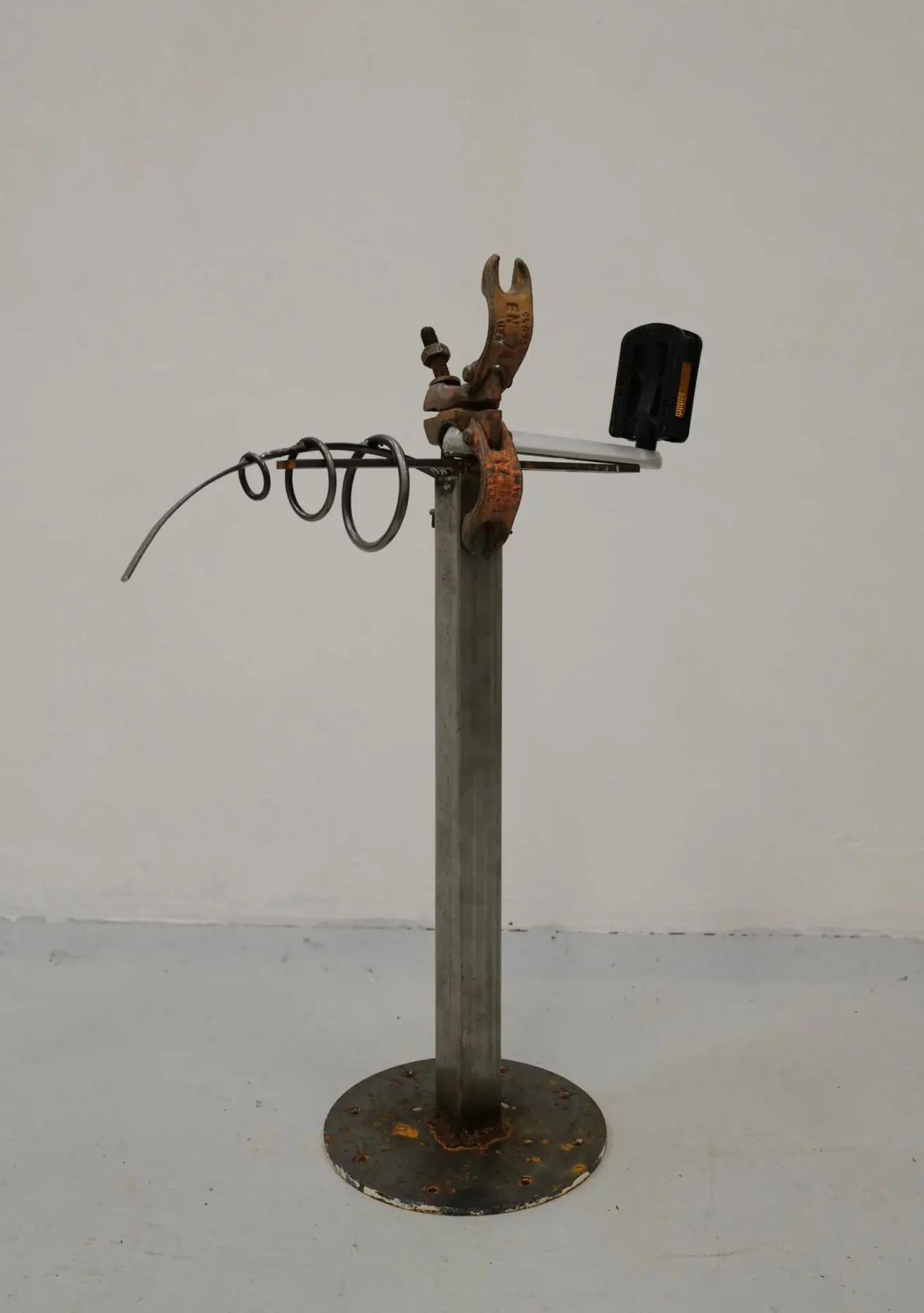 A metallic stand with various metal components like a clamp, rings, and a black rectangular object. The stand is on a gray floor.