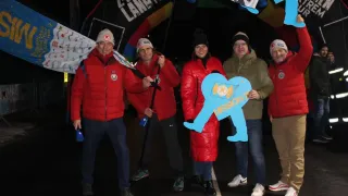 Five individuals in winter gear pose for a photo under a banner. They are smiling and appear to be participating in a marathon.