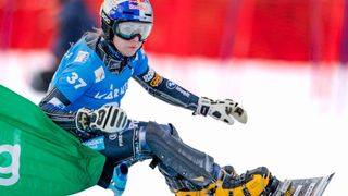 A skier wearing a blue and yellow suit, helmet, and goggles slides on a snow field. The skier wears gloves with white and blue colors and shoes with yellow and black colors.