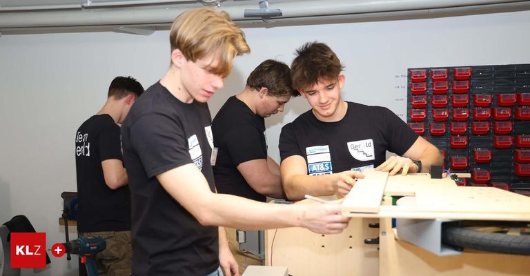 Fünf junge Männer in schwarzen T-Shirts arbeiten an einer Holzstruktur, einer hält einen Marker. Sie scheinen sich in einer Werkstatt zu befinden.