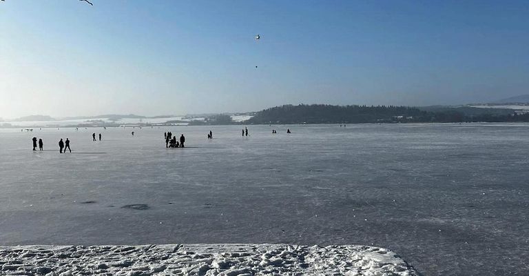 Ein gefrorener See mit mehreren verstreuten Personen und einem Hubschrauber, der im Himmel sichtbar ist.
