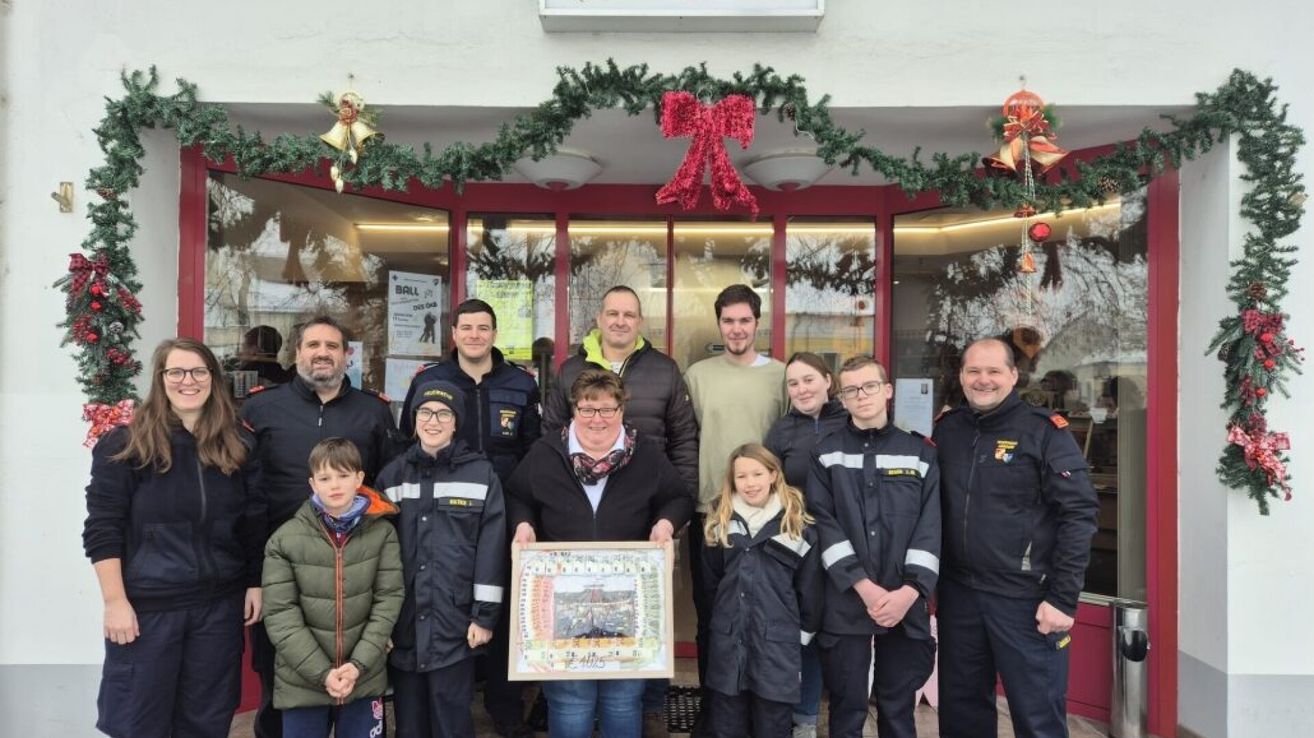 Eine Gruppe von Erwachsenen und Kindern steht vor einem Geschäft mit Weihnachtsdekoration. Eine Frau hält ein Zertifikat in der Hand.