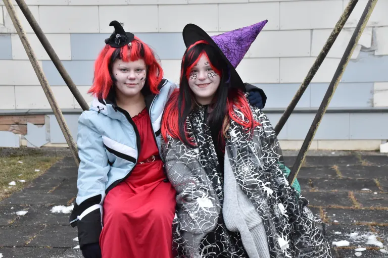 Two girls dressed as witches, one in a red dress and the other in a spider-themed outfit, pose for a photo.