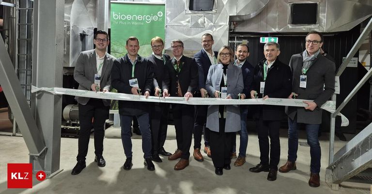 A group of people dressed in business attire holding a ribbon, standing in front of a building with a green banner reading bioenergie+ at.
