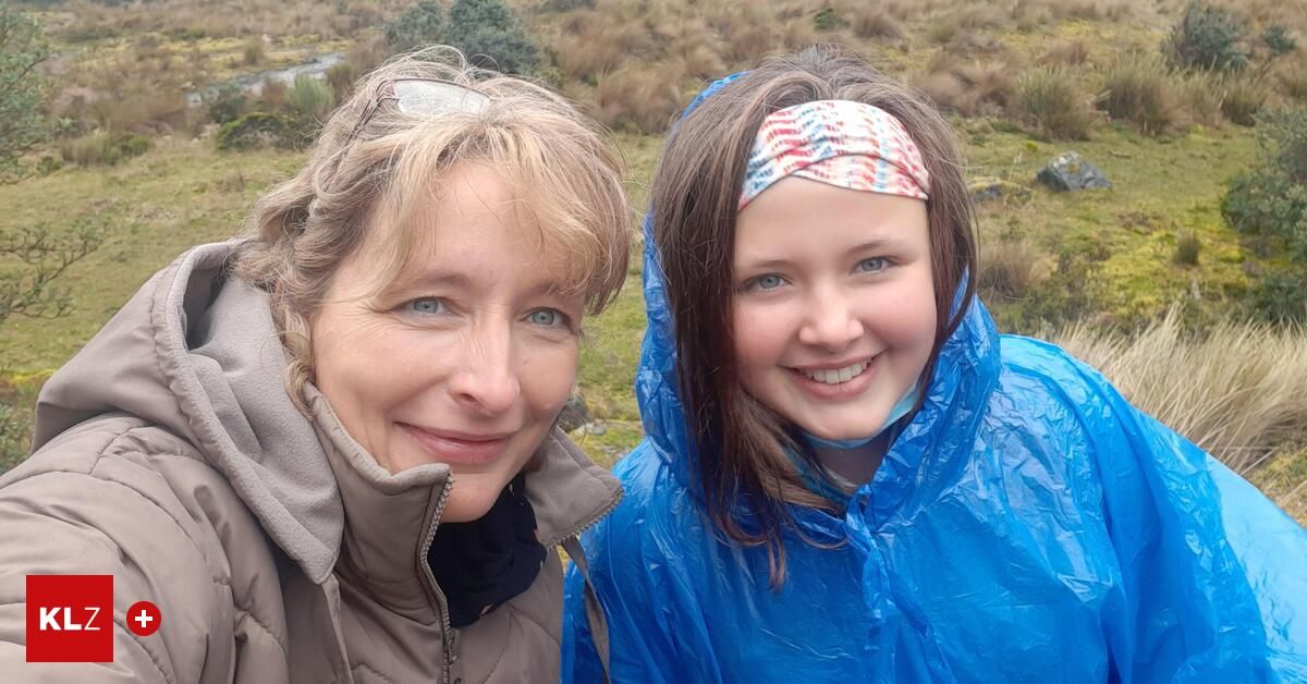 Two women are smiling for a photo in a grassy area. One has blonde hair and glasses on her head, the other has brown hair with a colorful headband.