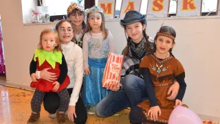 Eine Gruppe von Kindern in Kostümen für eine Party mit Dekorationen im Hintergrund. Ein Kind hält eine Tüte Popcorn.