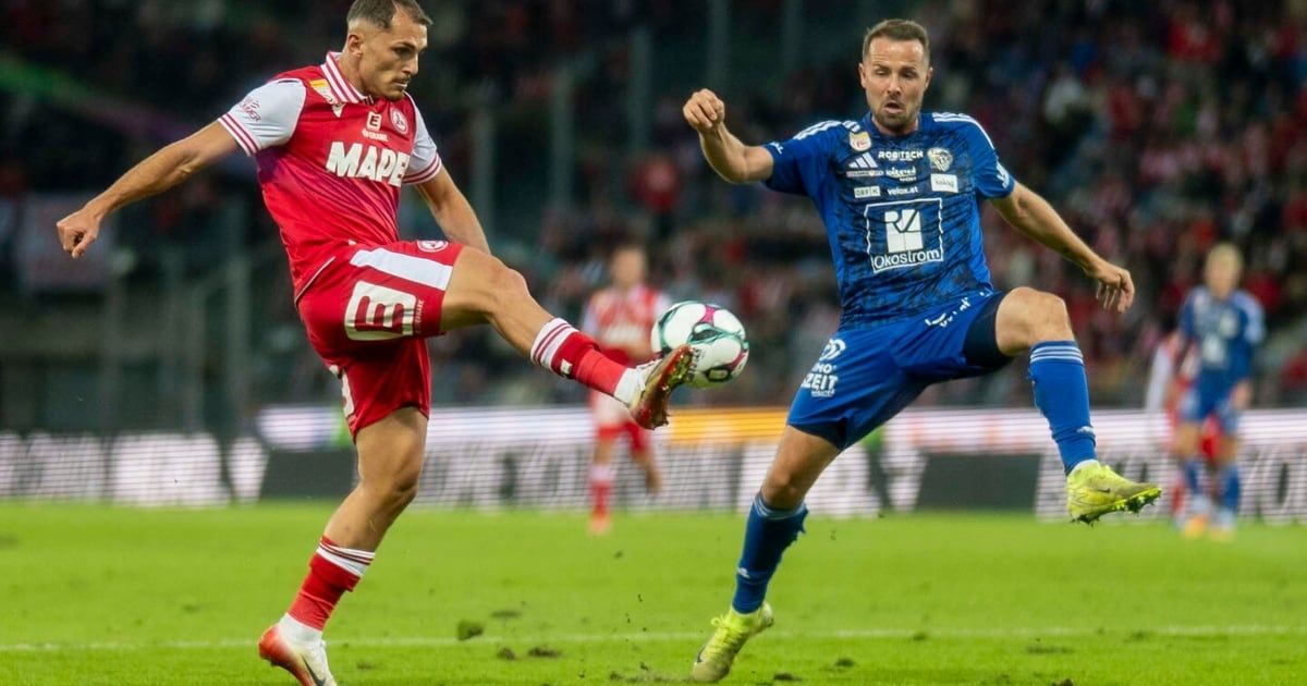 Two soccer players, one in red and the other in blue, compete for the ball during a match on a field.