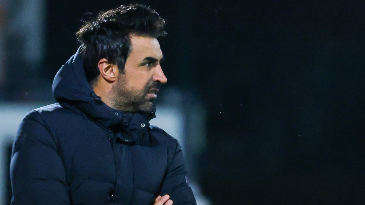 A man with a beard and mustache is wearing a navy blue jacket and appears to be looking forward.