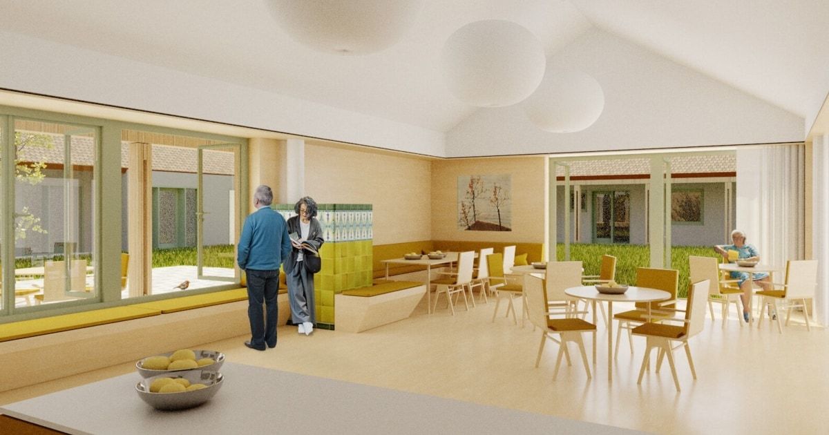 Eine Innenszene mit zwei Personen, eine liest, nahe einer Glastür. Ein Essbereich mit Tischen, Stühlen und einer Bank. Kunst an der Wand, runde Lampen an der Decke.