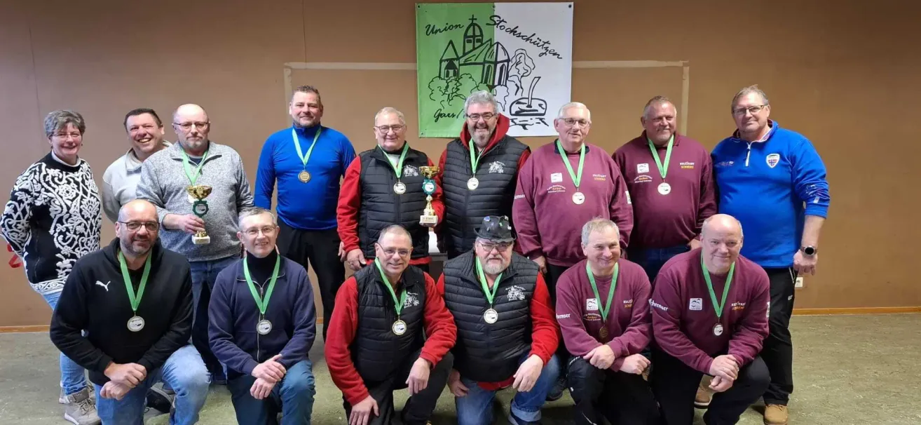 A group of men wearing vests and medals pose for a photo with a trophy. They are standing in front of a banner with the words Union Gars.