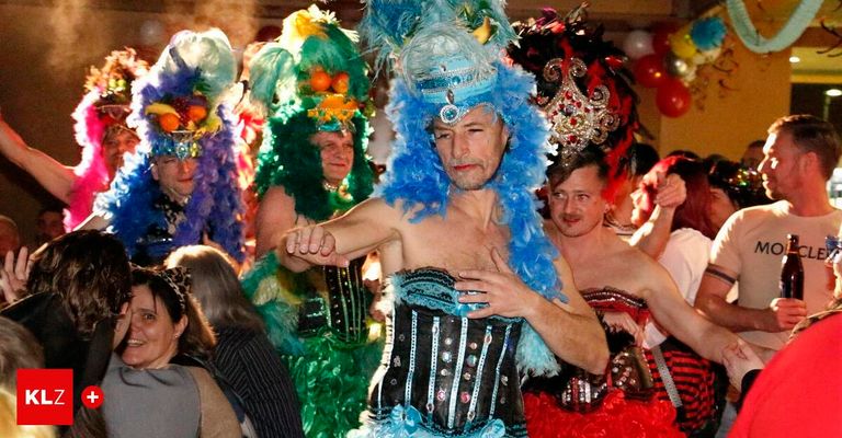 A group of people dressed in colorful costumes, possibly for a costume party, with one man in a blue feathery headdress and a black corset.