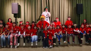 A group of children in red shirts and headbands, along with a man in a snowman costume, pose for a photo on a stage.