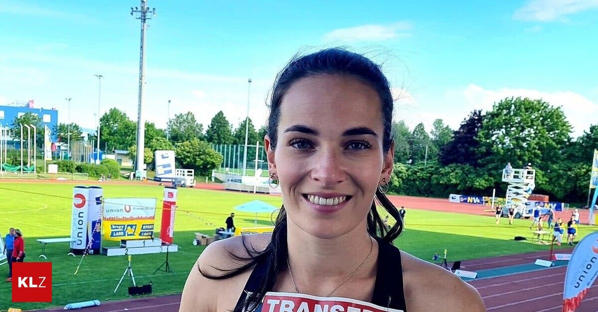 A woman wearing a black tank top with the word 'TRANSFER' on it is smiling and posing for a photo at an outdoor event. Behind her, a field is visible with people, tents, and trees.