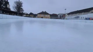 An empty outdoor ice rink surrounded by buildings. A tall streetlight is in the distance.