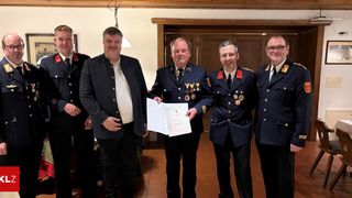 Five men in uniform, one holding a certificate, stand next to each other, smiling. They are in front of a wooden door.