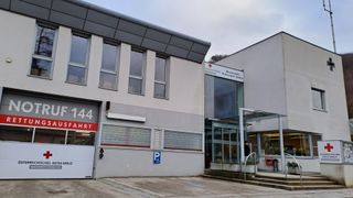 A white building with glass windows and red numbers 44 on the door, near a Red Cross sign and a glass wall with reflections.