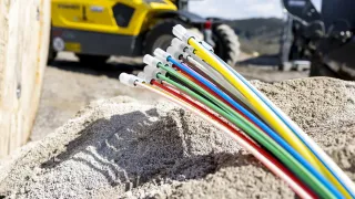 Bunte Kabel liegen auf einem Haufen Sand, mit einem gelben Baufahrzeug im Hintergrund.