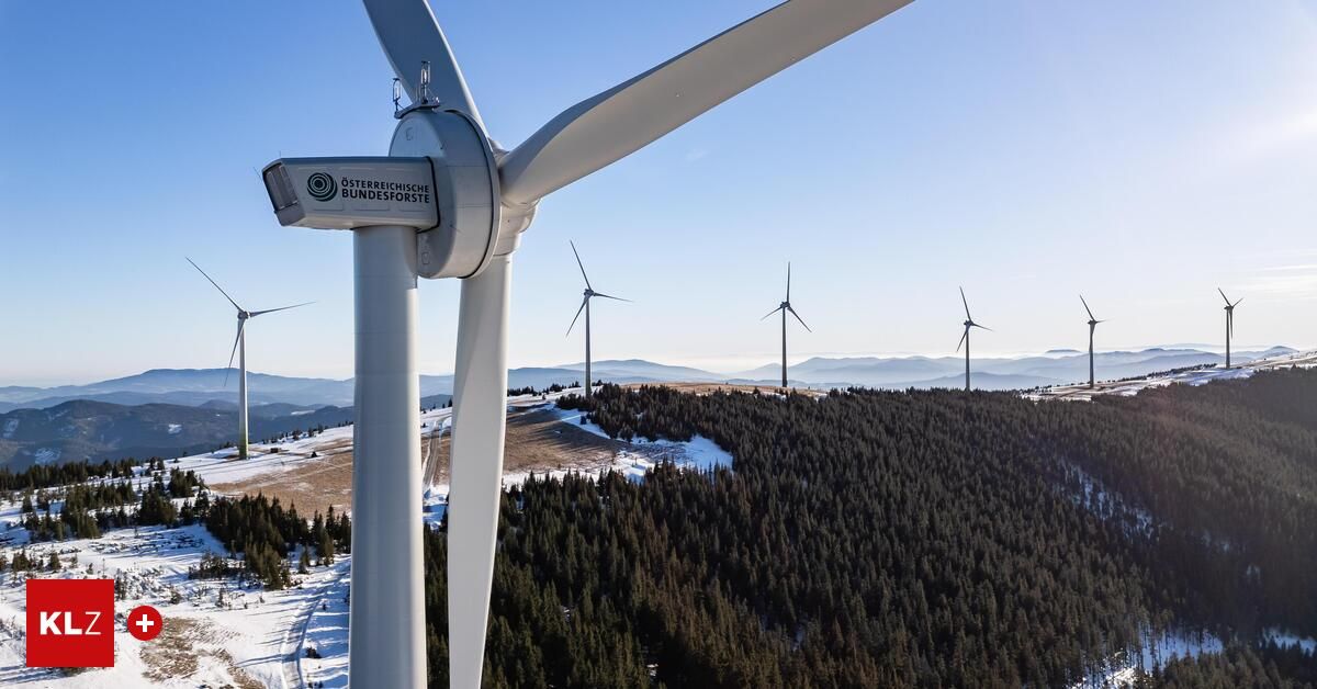 Aerial view of wind turbines in a snowy mountain area. Several turbines are visible, with one in the foreground featuring the logo of the Osterreichische Bundesforste.