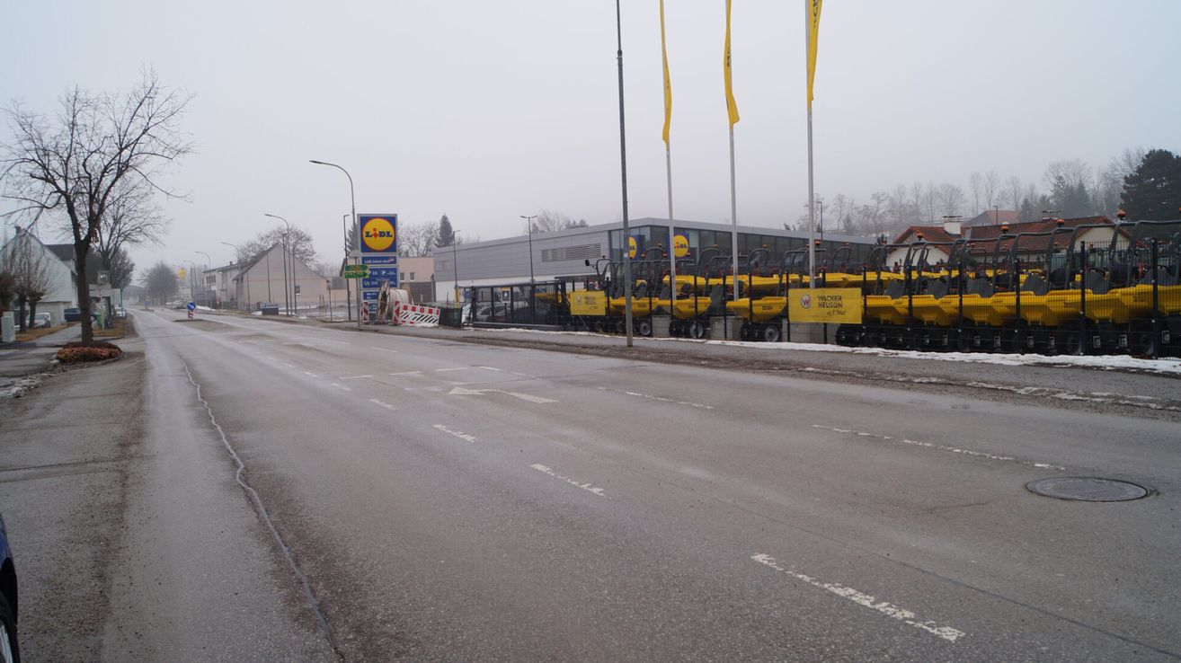 An empty street with fog in the distance. A LiDL sign is visible on the left, and several yellow Wacker Neuson vehicles are parked on the right.