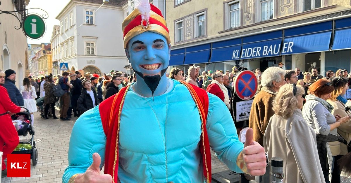A person dressed as a genie gives a thumbs up in a city square with many onlookers.