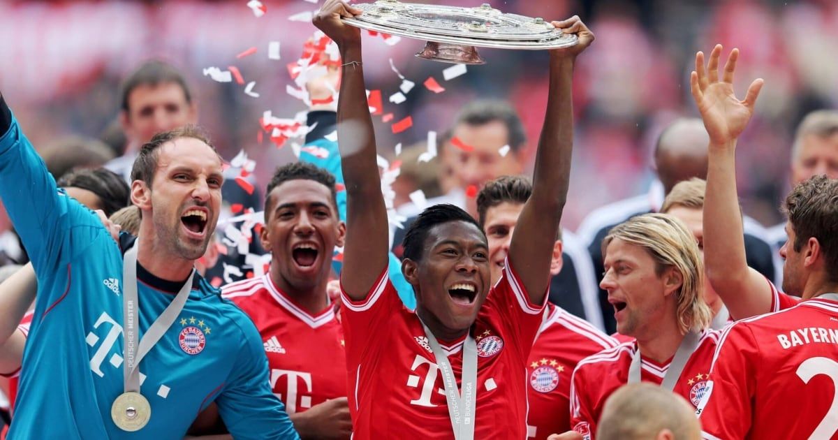 A soccer player in a red shirt holds a trophy in the air with confetti falling around him.