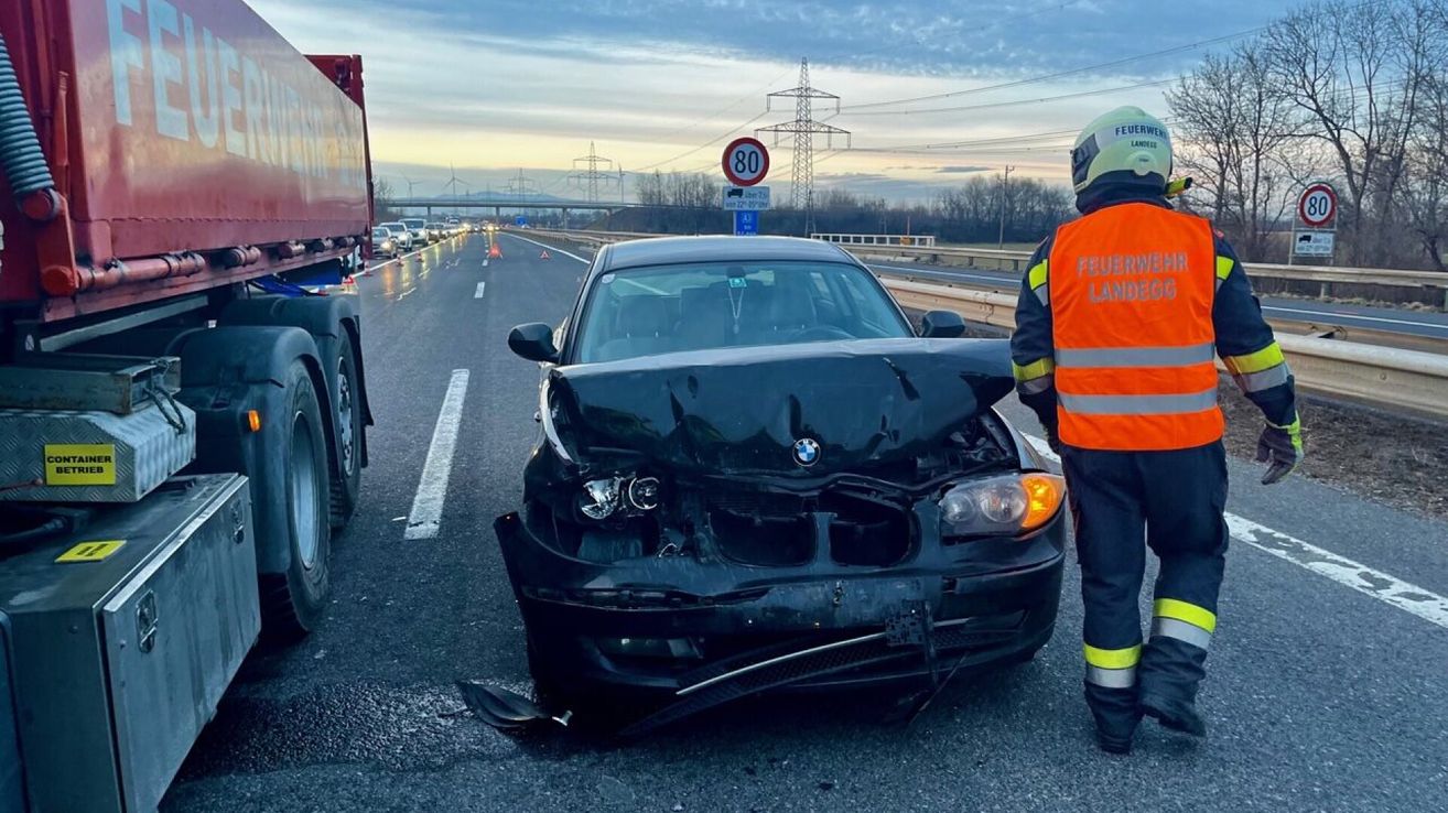 A damaged BMW car is parked on the side of a highway. A firefighter is standing nearby. The sky is cloudy.