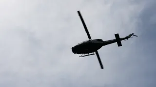 A black helicopter is flying in the sky with clouds. It has a long tail and two propellers. The sky is blue with white clouds.