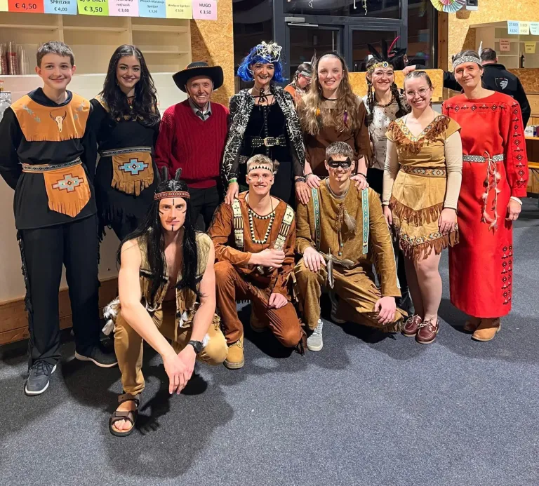 Eine Gruppe von Menschen in indianischer Kleidung posiert für ein Foto, mit einer Frau in Rot und einem Mann mit Hut in der Mitte.