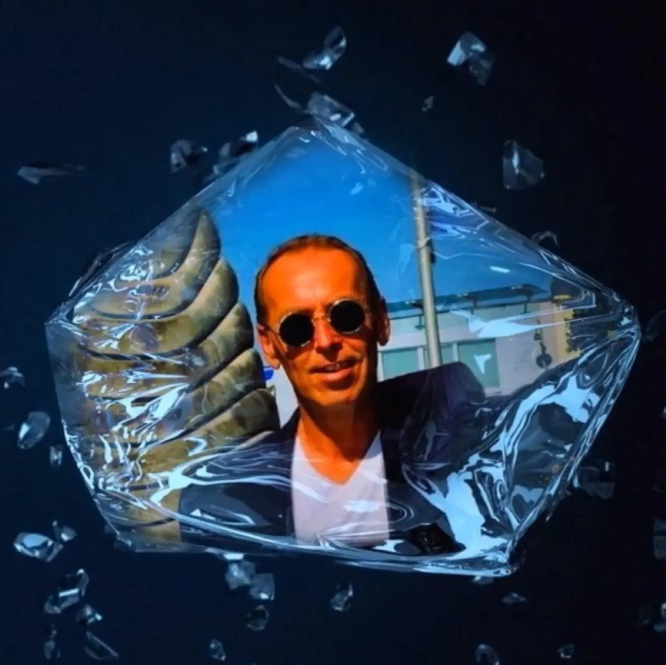 A man wearing sunglasses and a white shirt is inside a transparent ice cube, with his thumb up.