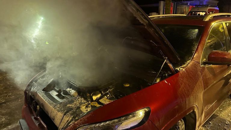 Ein rotes Auto mit geöffneter Motorhaube gibt weißen Rauch ab. Der Motor ist freigelegt, und der Rauch scheint aus dem Motorraum zu kommen.