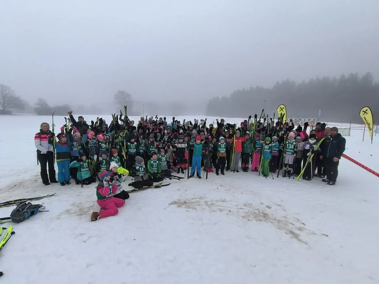 Eine Gruppe von Skifahrern in grünen und weißen Uniformen posiert für ein Foto im Schnee. Sie stehen und knien, halten Skistöcke und tragen Winterkleidung. Einige haben Nummern auf dem Rücken.