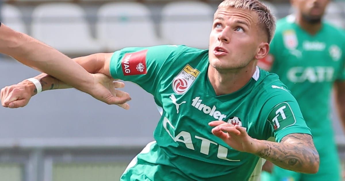 Ein Fußballspieler in einem grünen Trikot mit dem Wort 'tirler' darauf wird von einem anderen Spieler getackelt. Er hat einen ernsten Gesichtsausdruck.