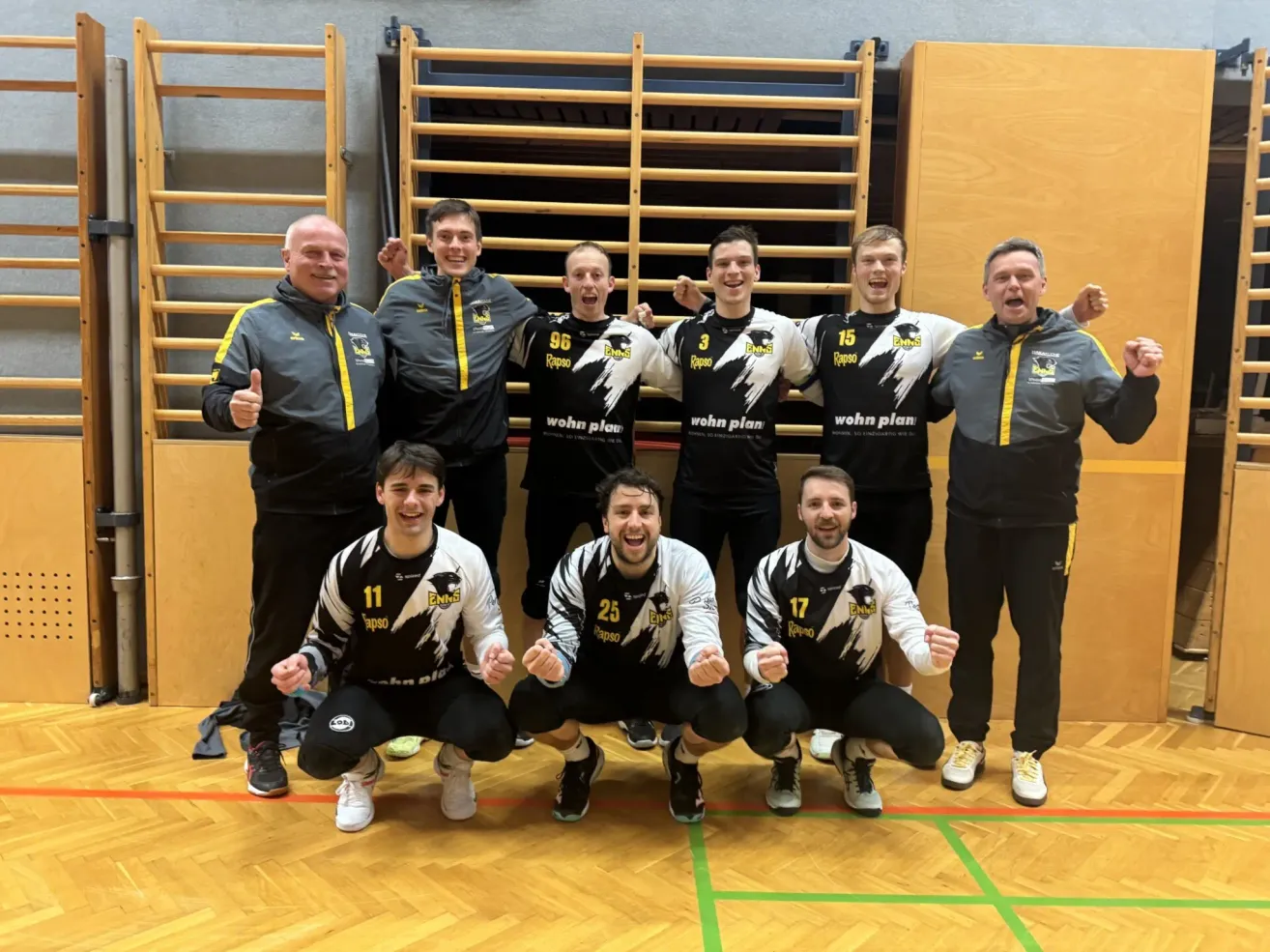 Eine Gruppe von Athleten, die in einem Fitnessstudio lächelnd und für ein Foto posieren. Sie tragen Uniformen mit Nummern. Der Hintergrund hat Holzwände und Ausrüstung.